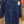 A dark navy blue work jumpsuit hanging on a wooden hanger in a retail store. The jumpsuit has a high collar, front button closure, and multiple utility pockets.