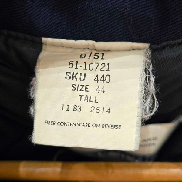 Close-up of a clothing size label sewn onto the inside neck of a dark navy garment, with a wooden hanger visible and part of a person's hand in frame.