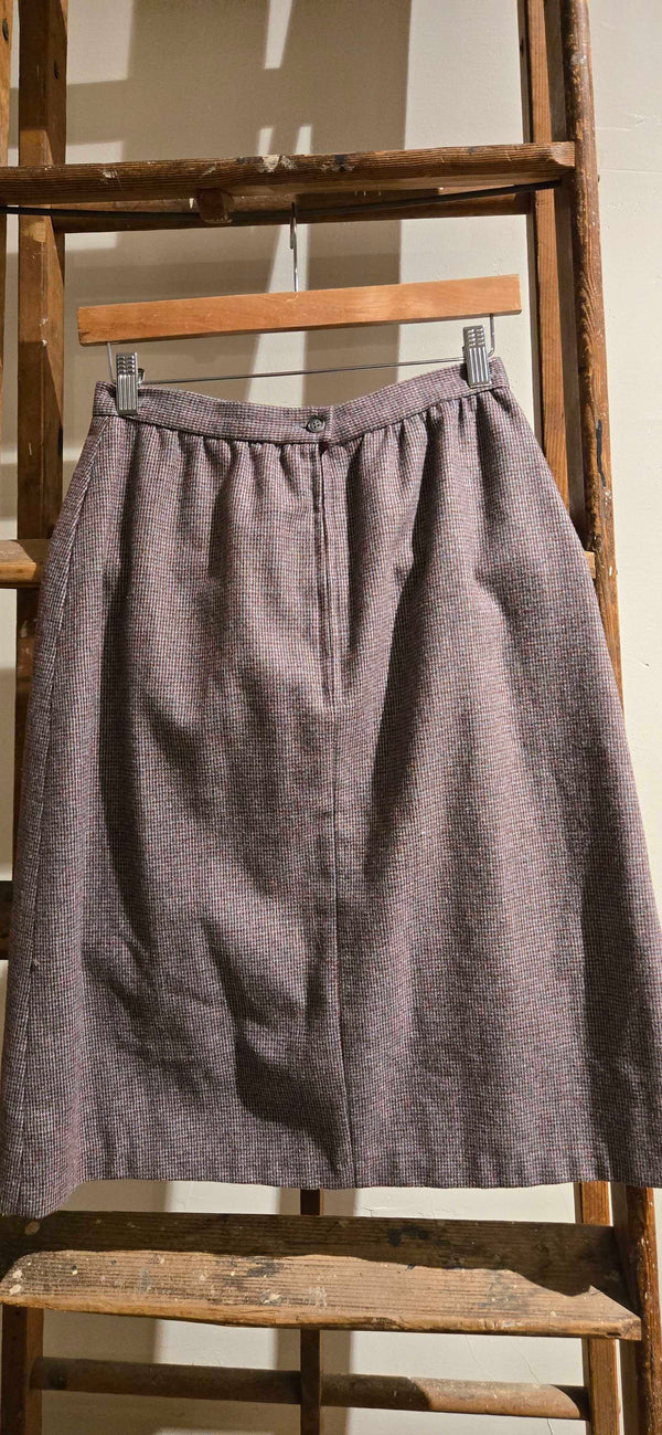 A textured, heathered grayish-purple skirt hanging on a wooden hanger from a rustic wooden ladder.