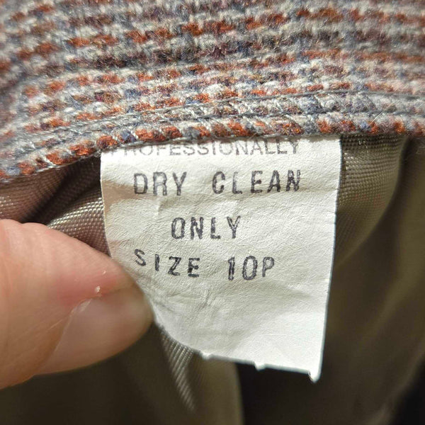 Close-up of a clothing size and care label sewn inside the collar of a tweed jacket, held by fingers. The label reads 'PROFESSIONALLY DRY CLEAN ONLY SIZE 10P'.
